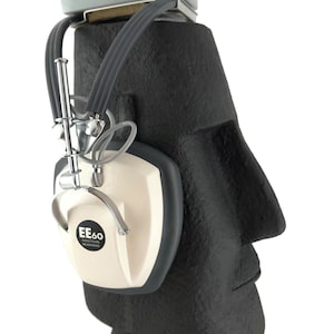 Pode incluir: Uma escultura de busto preta e cinza usando um par de fones de ouvido EE60 Tacticon brancos. Os fones de ouvido têm uma faixa de cabeça prateada e um microfone prateado.