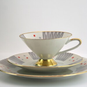 May include: A white teacup and saucer set with a grey and red geometric pattern and gold trim.