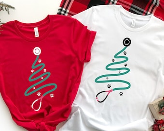 Könnte beinhalten: Zwei T-Shirts mit einem Weihnachtsbaum-Design aus einem Stethoskop und Pfotenabdrücken. Die T-Shirts sind rot und weiß. Der Text "ROT" und "WEISS" befindet sich in der oberen linken und rechten Ecke des Bildes.