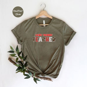 May include: A green t-shirt with the text "Very Merry Teacher" in red and white letters with a Christmas-themed pattern.