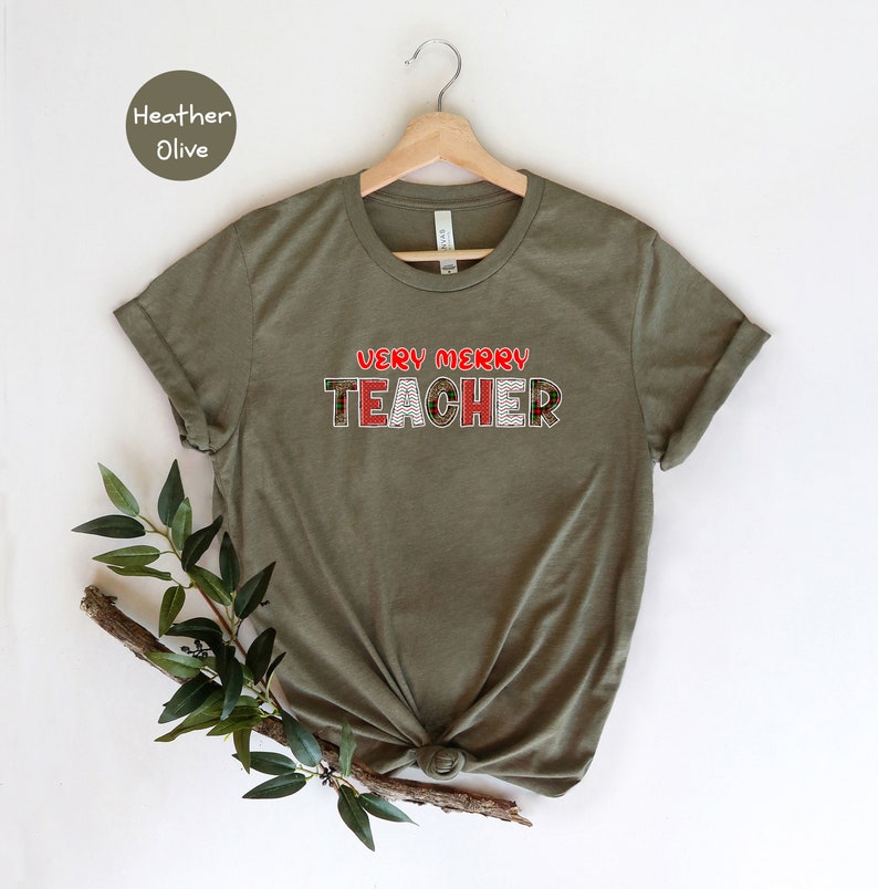 May include: A green t-shirt with the text "Very Merry Teacher" in red and white letters with a Christmas-themed pattern.