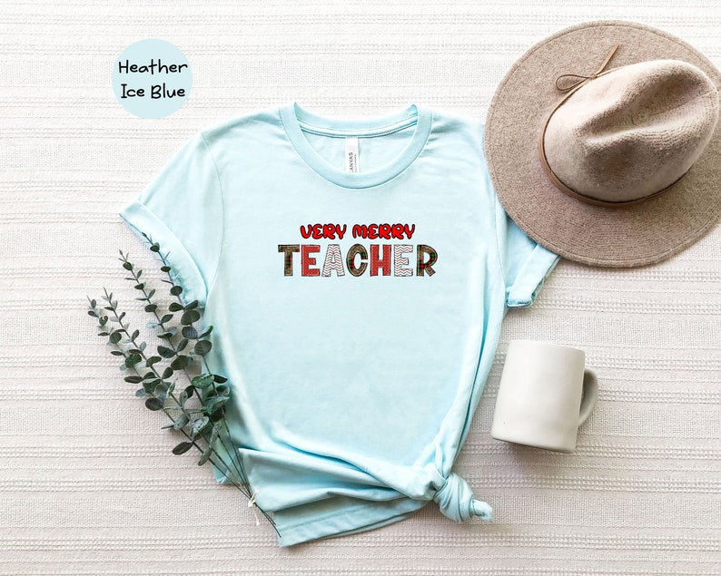 May include: Light blue t-shirt with the text "VERY MERRY TEACHER" in red and white letters with a Christmas-themed pattern.