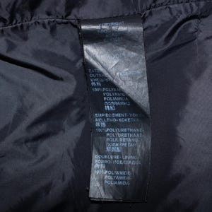 May include: Close-up of a black garment's interior, showcasing a tag with white text. The tag lists material composition, including 100% polyamide and polyurethane. The text is in multiple languages.