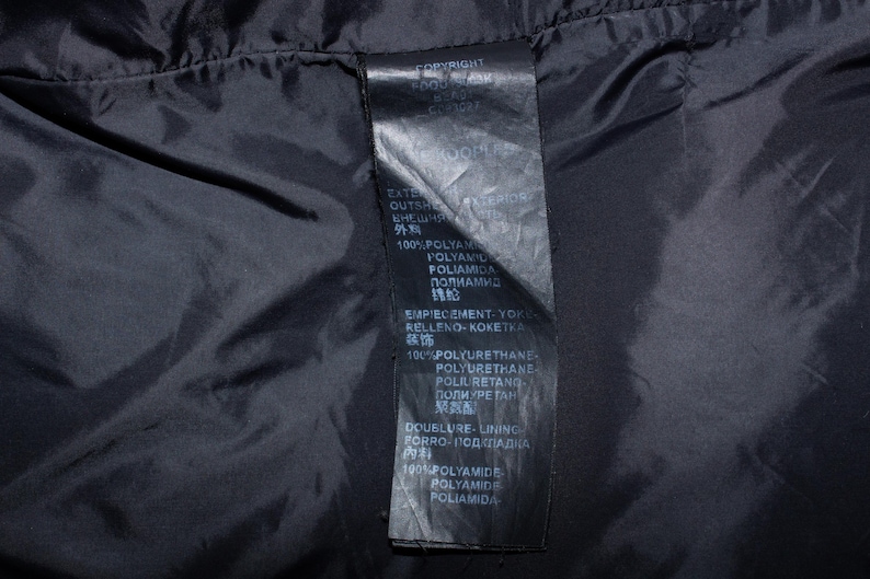 May include: Close-up of a black garment's interior, showcasing a tag with white text. The tag lists material composition, including 100% polyamide and polyurethane. The text is in multiple languages.