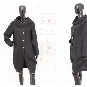 May include: A black linen coat with a large, gathered cowl neck and a button front closure. The coat has a relaxed fit and a slightly longer length.