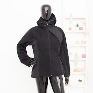May include: A black jacket with a hood, displayed on a mannequin. The jacket features a full-length zipper, a textured fabric, and contrasting smooth panels on the sides and shoulders. The mannequin is wearing black gloves.