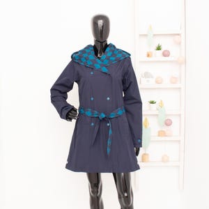 Può includere: Un cappotto blu navy con cappuccio e un motivo a scacchi sul cappuccio e sulla cintura. Il cappotto ha una chiusura a doppio petto e una cintura.