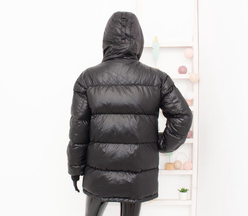 May include: Black puffer jacket with a hood. The jacket has a quilted design and a shiny finish. The jacket is a mid-length style, offering warmth and protection from the elements.