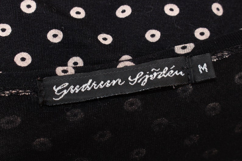 May include: A black fabric with a white polka dot pattern. A black label with white text reads "Gussaroen Sj&auml;zlen" and "M".
