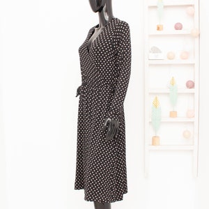 May include: A black midi dress with white polka dots. The dress has a V-neckline and long sleeves. It is cinched at the waist with a black belt.