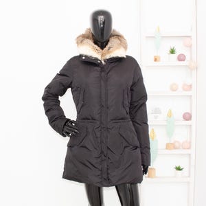 May include: A black winter coat with a fur-trimmed hood. The coat has a button closure, two front pockets, and a tailored fit. The mannequin is wearing black gloves and pants. The coat is displayed against a white background.