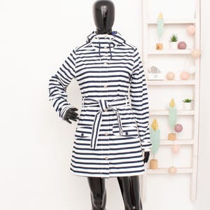 Può includere: Un impermeabile a maniche lunghe con un motivo a righe orizzontali blu navy e bianco. La giacca presenta un cappuccio con coulisse regolabile, una chiusura frontale con bottoni e una cintura in tessuto abbinata in vita con due tasche.