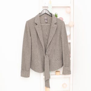 May include: A black and white houndstooth blazer with a tie detail at the front. The blazer has long sleeves and a classic collar.