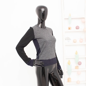 May include: A long-sleeved shirt with a black, grey, and navy blue colour block design. The shirt has a crew neck and a relaxed fit.