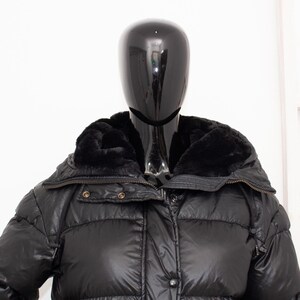 May include: Black puffer jacket with a faux fur collar. The jacket has a quilted design and a zipper closure. The mannequin is wearing the jacket. The jacket is a winter coat.
