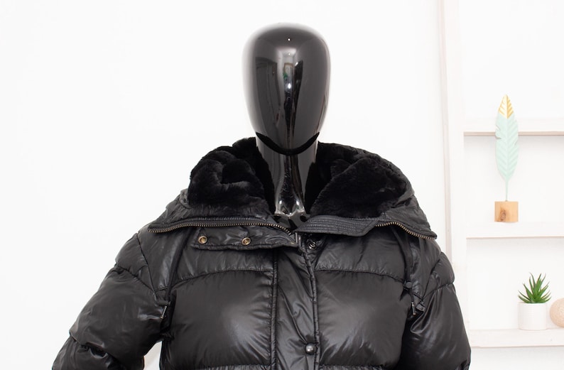 May include: Black puffer jacket with a faux fur collar. The jacket has a quilted design and a zipper closure. The mannequin is wearing the jacket. The jacket is a winter coat.