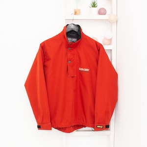 Könnte beinhalten: Leuchtend rote Gavin Green Jacke mit schwarzem Kragen und Knopfverschluss. Die Jacke hat lange Ärmel und den Text "Gavin Green" auf der Brust. Der Ärmel hat auch den Text "GORE-TEX".