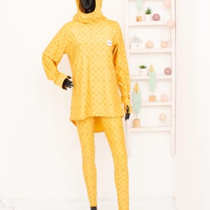 Peut inclure: Un haut à manches longues jaune à capuche et un legging assorti avec un motif géométrique. Le haut a un col montant et le legging est ajusté.