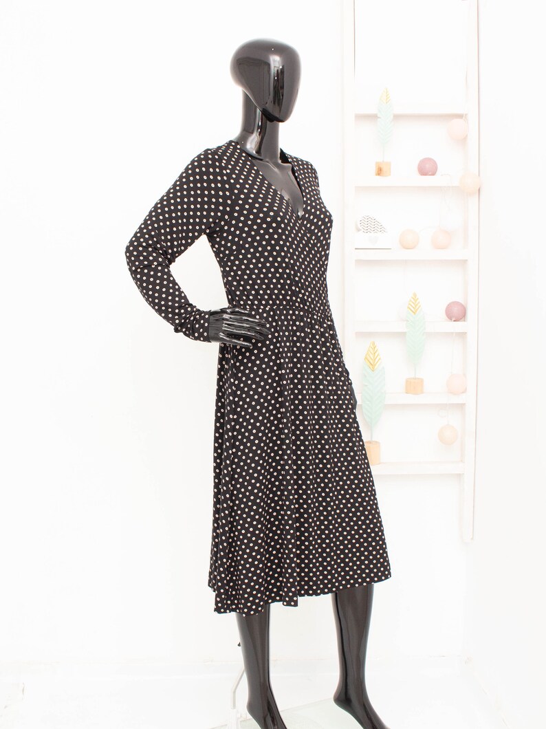 May include: A black midi dress with white polka dots. The dress has long sleeves and a v-neckline.
