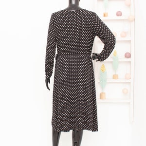 May include: A black midi dress with white polka dots. The dress has long sleeves and a V-neckline.