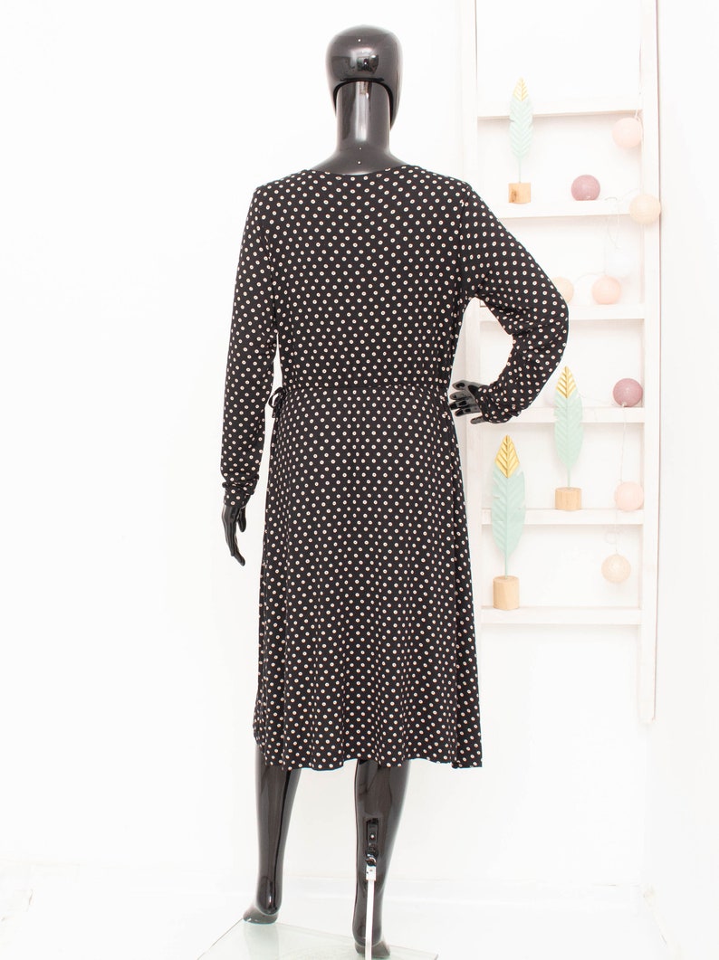 May include: A black midi dress with white polka dots. The dress has long sleeves and a V-neckline.