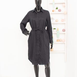 May include: A black linen shirt dress with a button-up front and a tie belt at the waist.