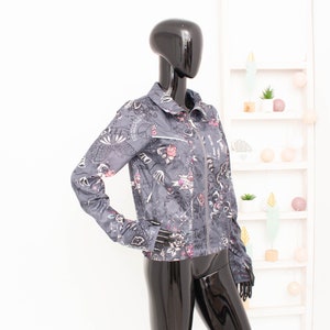 May include: A grey jacket with a colourful print of flowers, peace signs, and other designs. The jacket has a zip closure and a collar.