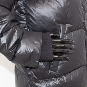 May include: A shiny black puffer jacket with a quilted design. The jacket features a ribbed knit cuff and a pocket detail. The material has a glossy finish, reflecting light. The jacket is designed for cold weather.