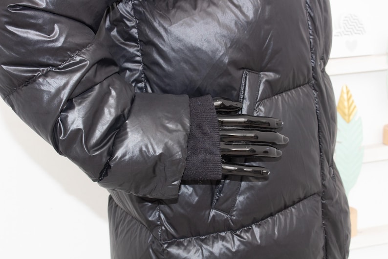 May include: A shiny black puffer jacket with a quilted design. The jacket features a ribbed knit cuff and a pocket detail. The material has a glossy finish, reflecting light. The jacket is designed for cold weather.