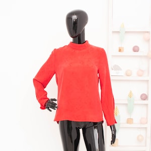 May include: A red long-sleeved blouse with a mock neck and a textured fabric.