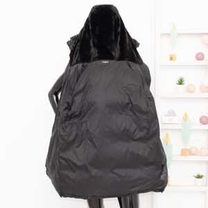 May include: A black winter coat with a faux fur-lined hood. The coat is open, revealing a quilted interior. The coat is displayed on a mannequin. The background includes a white shelf with decorative items.