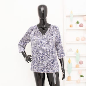 Peut inclure: Un chemisier à motifs bleus et blancs avec un col en V et des manches trois-quarts. Le chemisier est présenté sur un mannequin noir. Le motif a un design en peau de serpent. Le chemisier est un haut décontracté.