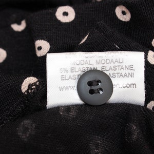 May include: A white fabric tag with black text that reads "Modal, Modaaali 95% Elastan, Elastane, Elasto Astaan, www.en.com". A black button is attached to the tag.