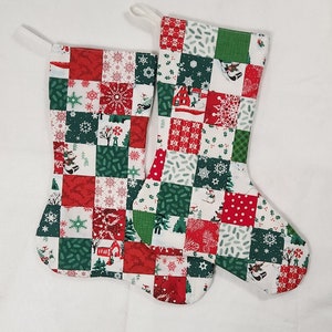 Peut inclure: Deux chaussettes de Noël rouges et vertes avec un motif patchwork. Les chaussettes présentent des flocons de neige, des sapins et d'autres motifs sur le thème de l'hiver.