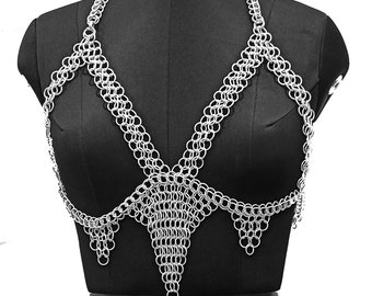 May include: A silver chainmail bra top on a black mannequin. The bra top has a V-shaped design in the centre and is made of small, interlocking metal rings.
