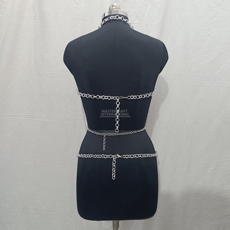 May include: A silver-toned metal chain body harness featuring a choker collar, a horizontal chest chain, and a waist chain, all connected by vertical links. The text MASTER CRAFT INTERNATIONAL is visible in the center of the chest area.
