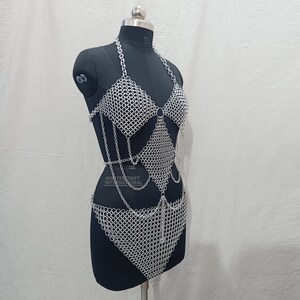 May include: A silver-toned chainmail body harness featuring a halter-style top, a diamond-shaped midsection panel, and a triangular lower section, all constructed from interlocking metal rings. The text MASTERCRAFT INTERNATIONAL is visible.