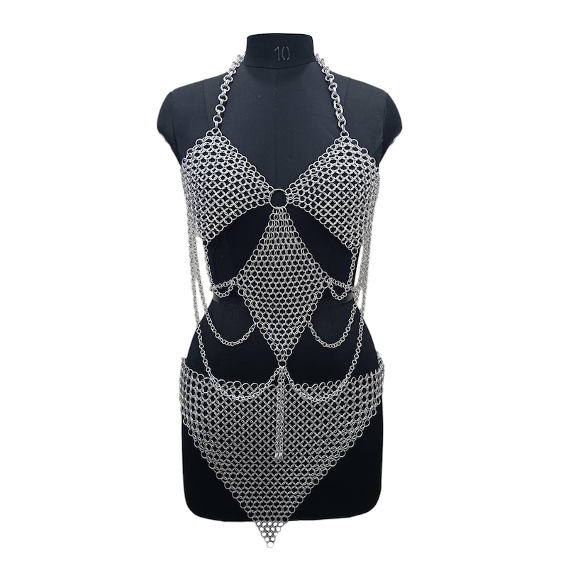 May include: A silver-toned chainmail body harness constructed from interlocking metal rings. The design features a halter-style neckline, two triangular chest panels, a diamond-shaped midsection, and a pointed lower section with draped chain accents.