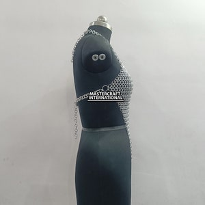 May include: Silver chainmail top with a halter neckline. The top is displayed on a black mannequin. The text "MASTERCRAFT INTERNATIONAL" is visible on the top.