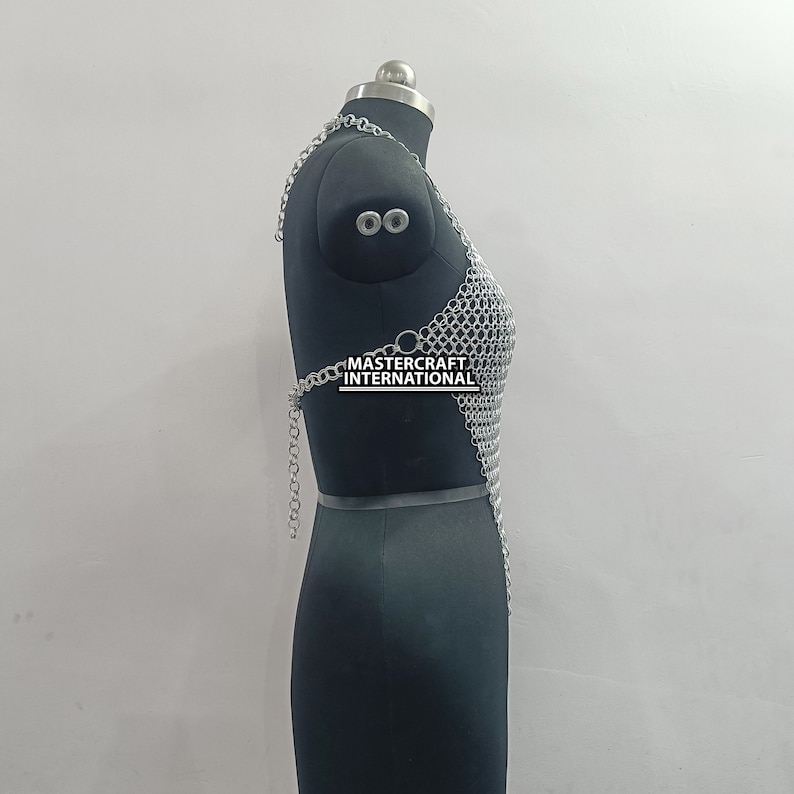 May include: Silver chainmail top with a halter neckline. The top is displayed on a black mannequin. The text "MASTERCRAFT INTERNATIONAL" is visible on the top.
