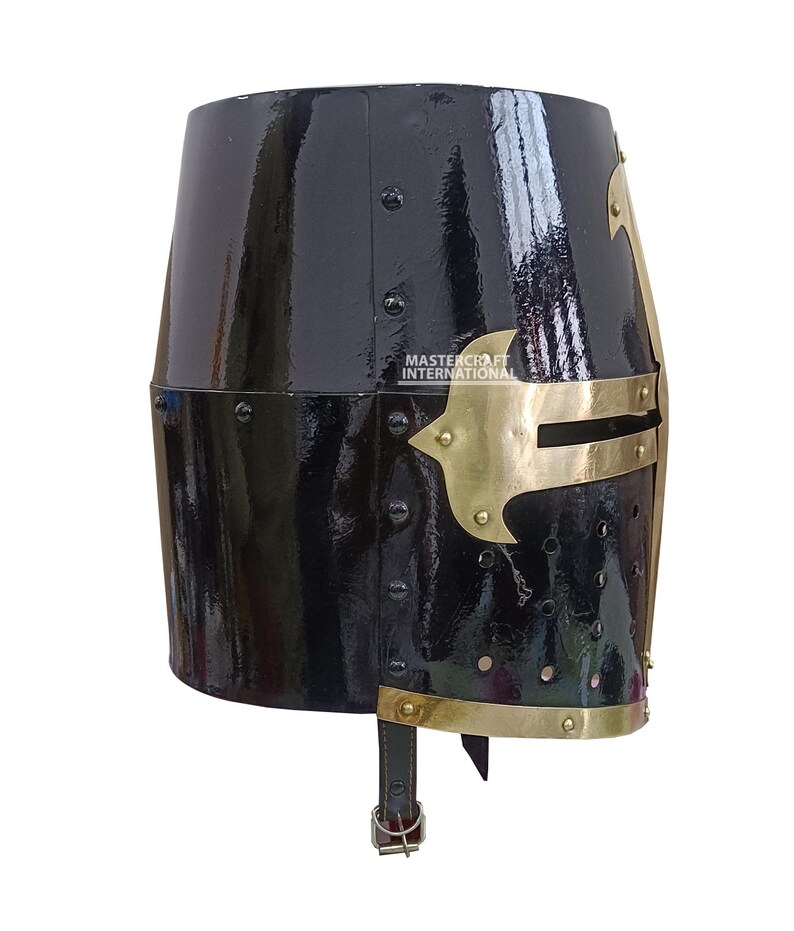 Op de afbeelding: Een zwarte, glanzende ridderhelm met messing details. De helm heeft een geklonken constructie en een messing frontplaat. De tekst "MASTERCRAFT INTERNATIONAL" is zichtbaar. Een leren riem met een gesp is bevestigd.