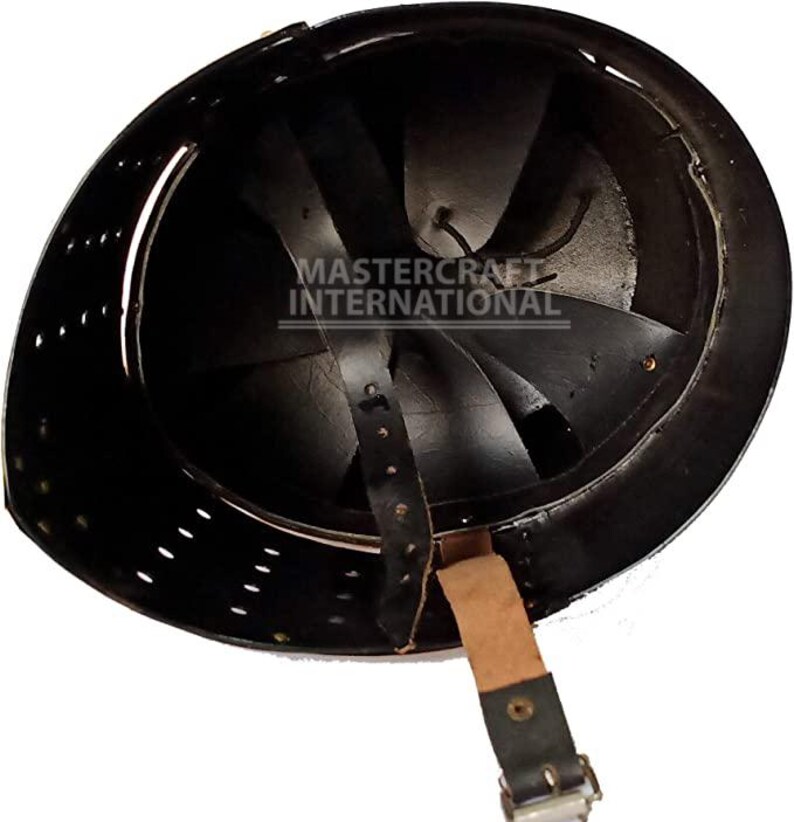 Op de afbeelding: Zwarte metalen helm met binnenvoering en kinband. De binnenkant heeft een reeks gebogen metalen platen. De helm heeft kleine ventilatiegaten rond de rand. De tekst "MASTER CRAFT INTERNATIONAL" is zichtbaar in de helm.