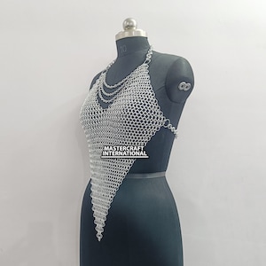 May include: Silver chainmail top with a V-neckline and a pointed hem. The top is made of small, interlocking metal rings. The text "MASTERCRAFT INTERNATIONAL" is visible on the top.