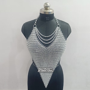 May include: Silver chainmail top with a halter neckline and a pointed bottom. The top is made of small, interconnected metal rings. The label "MASTERCRAFT INTERNATIONAL" is visible on the bottom of the top.