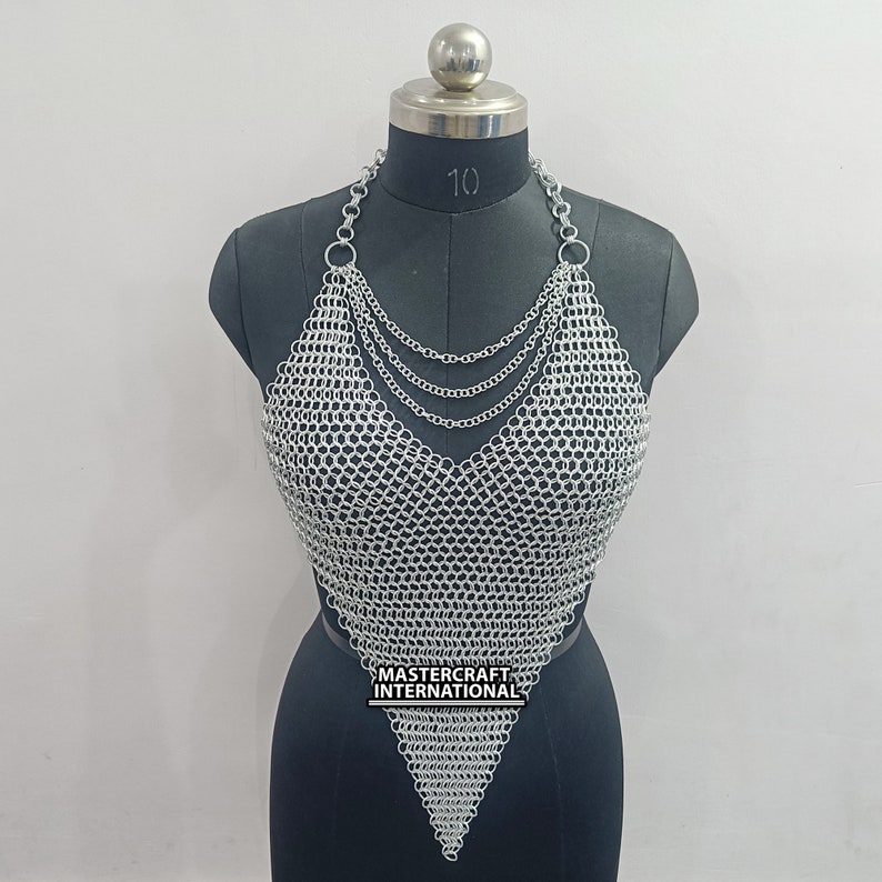 May include: Silver chainmail top with a halter neckline and a pointed bottom. The top is made of small, interconnected metal rings. The label "MASTERCRAFT INTERNATIONAL" is visible on the bottom of the top.