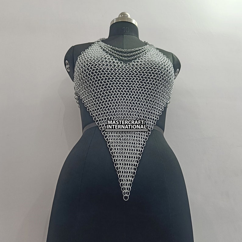 May include: A silver chainmail top with a triangular shape. The top is on a black mannequin and has a black belt with the text "MASTERCRAFT INTERNATIONAL" on it.