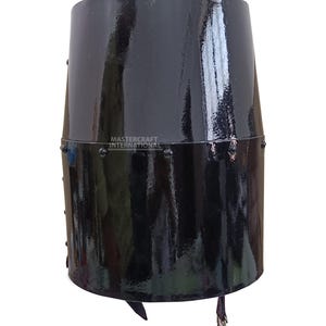 Op de afbeelding: Een zwarte, cilindrische helm met een glanzende afwerking. De helm heeft een geklonken band en een leren riem met een gesp. De tekst "MASTERCRAFT INTERNATIONAL" is zichtbaar. Historisch item.