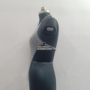 May include: Silver chainmail top with a halter neckline and a triangular shape. The top is displayed on a black mannequin. The text "MASTERCRAFT INTERNATIONAL" is visible on the top.