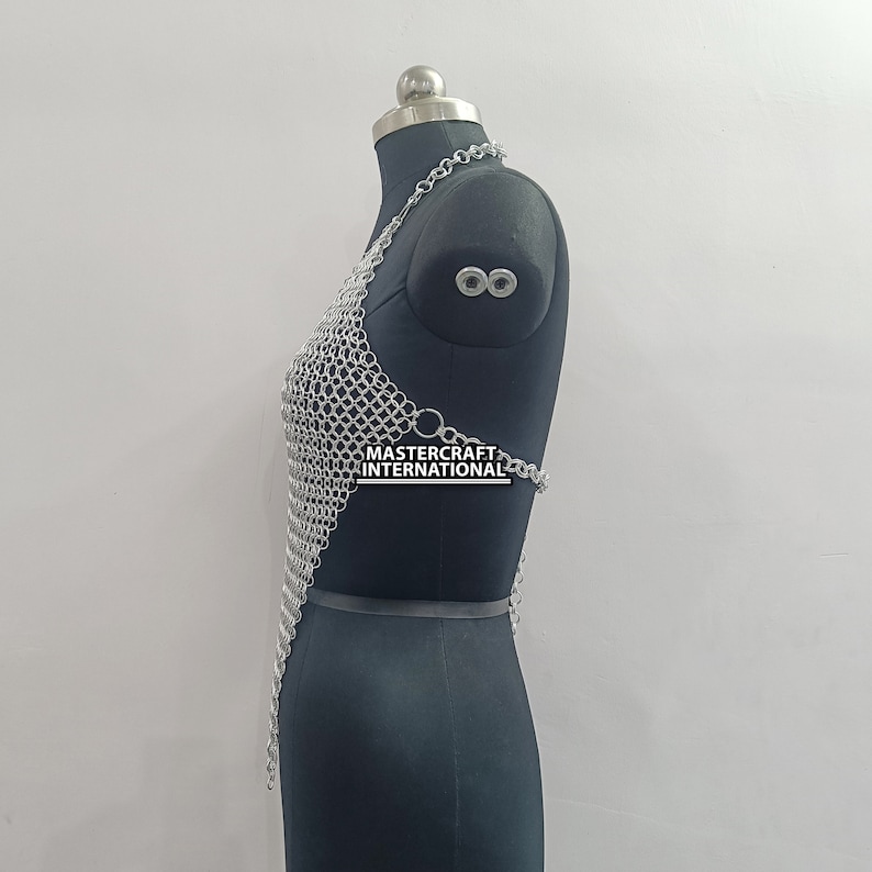 May include: Silver chainmail top with a halter neckline and a triangular shape. The top is displayed on a black mannequin. The text "MASTERCRAFT INTERNATIONAL" is visible on the top.