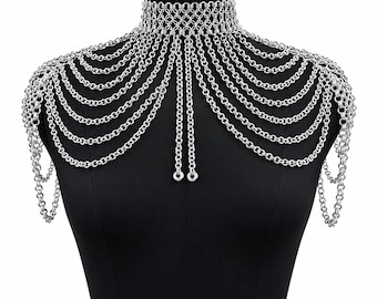 May include: A silver-toned chainmail shoulder necklace featuring a high-neck choker collar constructed from interlocking metal rings. Multiple draped silver chains extend from the collar across the chest and shoulders, ending in two vertical strands.
